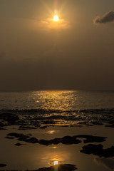 A portrait shot of the Indian Ocean and rocky beach of Neil island with sun and its reflection