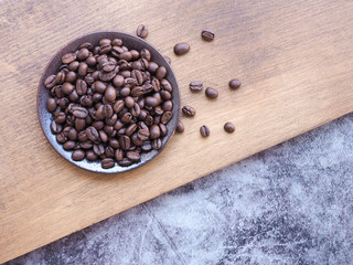 Roasted coffee beans in a brown plate on rusty wood over grey background with copy space for text. View from above.