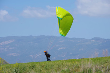 A paraglider moments before lift off from a high elevation meadow with a mountain ridge and blue sky with some clouds in the background