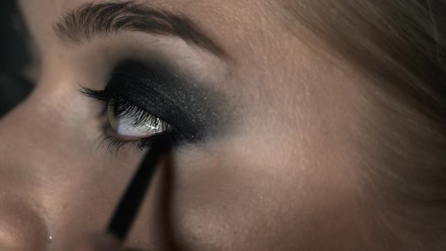 Macro shot of makeup artist making professional make-up for young woman in beauty studio. Make up Artist makes the makeup smokey eyes of a black shade with special brush of a beautiful model