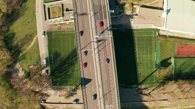 Aerial drone top view of epic highway bridge with a lot of traffic. The bridge is running over a strangely placed soccer/football field. Abstract concept of modern transportation and engineering.
