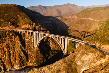 Big Creek Bridge in Big Sur, California. The photo is taken aerially from a drone as the sunsets in the distance, creating beautiful light on the bridge.