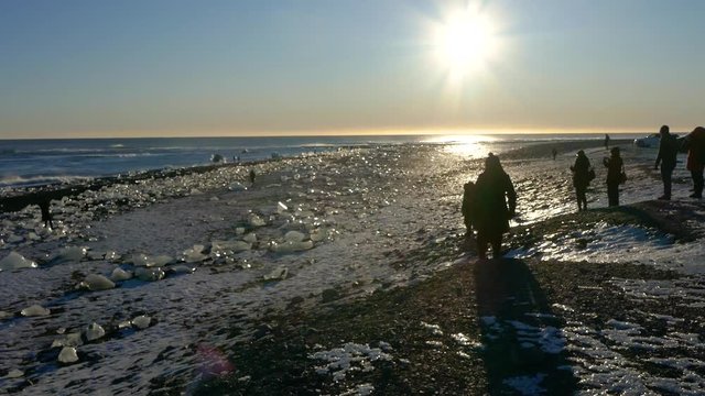 Silhouette unrecognizable people visiting iceberg ice chunks on black sand beach