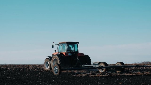 a tractor in a field in spring drags black soil against a clear blue sky. Work in the field on agricultural machinery. Preparation for sowing the field.