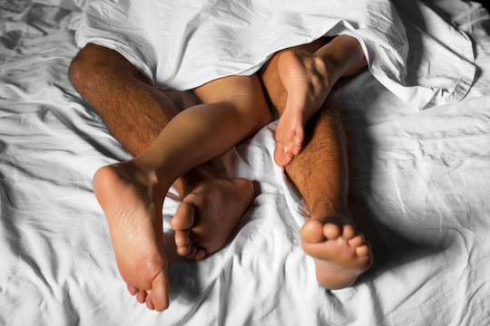 Legs of loving couple cuddling in bed under the sheets