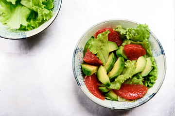 Avocado grapefruit salad with lettuce in a bowl on grey metal background. Raw vegetarian detox salad, healthy food. Selective focus