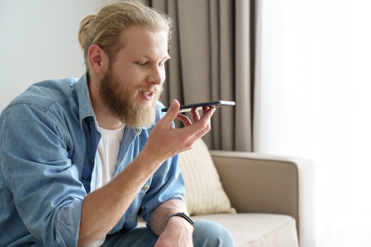 Young Man Holding Smart Phone Speak On Speakerphone, Using Virtual Digital Voice Recognition Assistant Search, Record Audio Message On Smartphone At Home. Mobile App Ai Digital Tech Assistance Concept