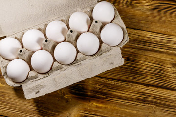 Raw chicken eggs in cardboard egg box on wooden table. Top view