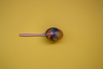 Single colorful egg in wooden spoons isolated on yellow background, one multicolored egg, Easter tradition, celebration concept