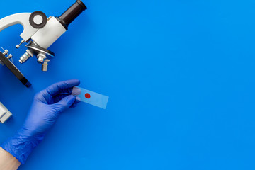 Bood testing with microscope in laboratory. Sample in hands on blue background copy space