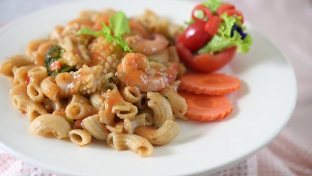 Stir fried macaroni with shrimp, squid, tomatoes, peppers and broccoli on a white plate
