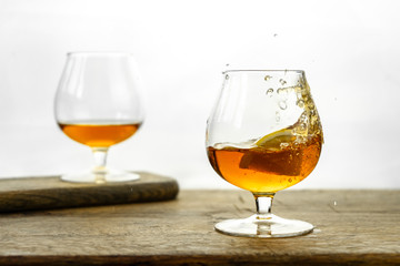 Cognac \ whiskey in cognac glass on wooden table, golden color spirits splashing on white background