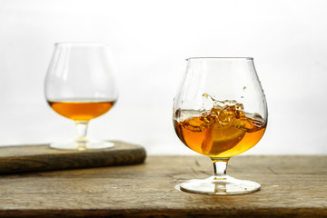 Cognac \ whiskey in cognac glass on wooden table, golden color spirits splashing on white background