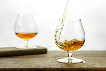 Cognac \ whiskey in cognac glass on wooden table, golden color spirits splashing on white background