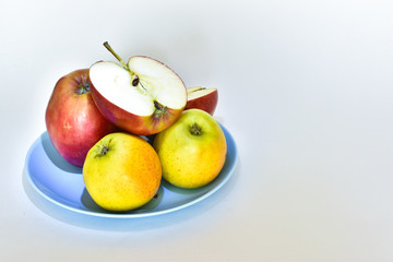 
red and yellow apples lie on a blue plate on the table, on a white background