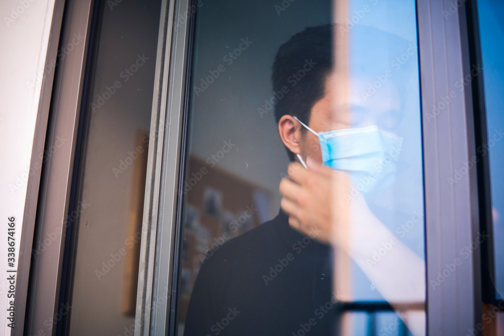 Wall mural quarantine self-isolation. sad young man in a medical mask who looks out the window through the wind