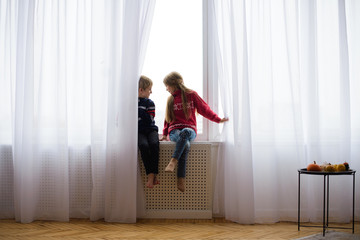 brother and sister are sitting on windowsill, near window glass, they want to walk on street, but in world there is  coronavirus pandemic, and they remain at home