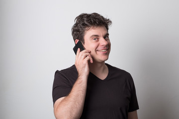 Man is talking on a cell phone. Smiling young man in a black T-shirt talking on the phone.