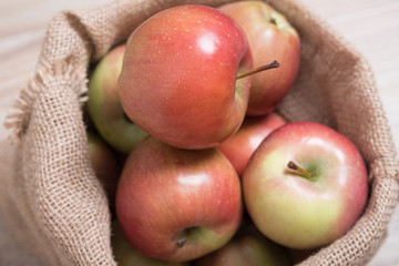 Bag with apples. Studio image. Red apples in a burlap bag on a wooden background. Fabric bag full of apples.