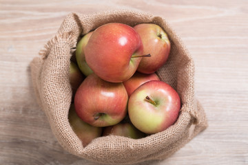Bag with apples. Studio image. Red apples in a burlap bag on a wooden background. Fabric bag full of apples.