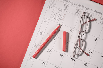 Closeup of a red pen and glasses on a open calendar. Calendar open on a august page on a red background.