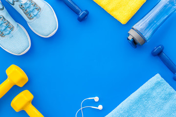 Fitness set with sneakers, dumbbells, towel on blue background top view copy space
