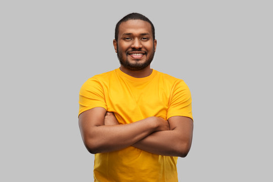 people concept - smiling young african american man in yellow t-shirt with crossed arms over grey background