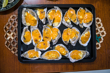 Oysters in a pan in a creamy sauce and cheese. Against a table background