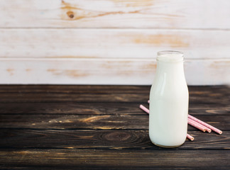 Fresh milk, in a glass bottle on a black wooden background with pink drink tubes.