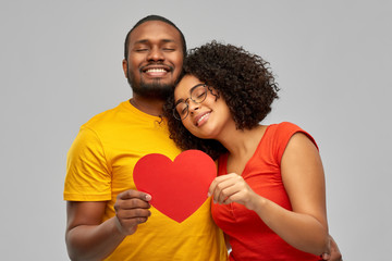 love, relationships and valentines day concept - happy african american couple holding big red paper heart over grey background