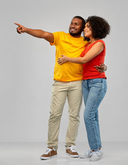 Obraz premium relationships and people concept - happy smiling african american couple pointing finger to something over grey background