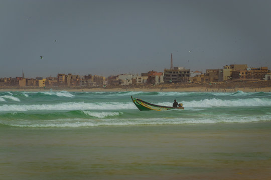 A lone fishermen is riding his pirogue or piraga, a typical senegalese fishing boat just ashore of the beach in Yoff, Dakar.