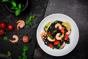 Black Pasta - Squid Ink, with Prawns, Seafood,Lemon and Tomatoes in White Bowl on  Dark Background. Top view.