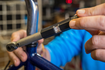 Tightening of a bicycle seat post with the use of a small torque wrench. Proper way to tighten a bicycle seatpost. Bicycle service in a worshop. - obrazy, fototapety, plakaty