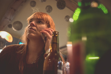 Young concerned woman in a bar with drinks on the table using a telephone. Concept of drunk woman...