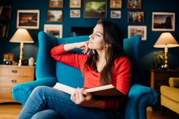Woman thinking while reading a book at home,being distracted by her thoughts.Concentration...