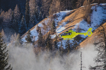 A yellow rescue helicopter is taking of in the middle of the ski slope area in a big cloud of snow. Concept of helicopter rescue on snow or ski slope.
