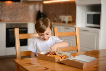 The boy smiles and sorts dried fruits in a box sitting in the kitchen