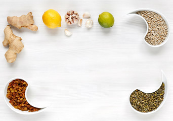 Orange, ginger, garlic, lime, lemon, raisins, sunflower seeds, pumpkin seeds lie on a white wooden surface, top view. Organic, vegetarian products that increase the body's immunity.