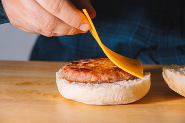 Man hands putting on top of a burger a slice of cheese on a wooden board. Cooking concept.