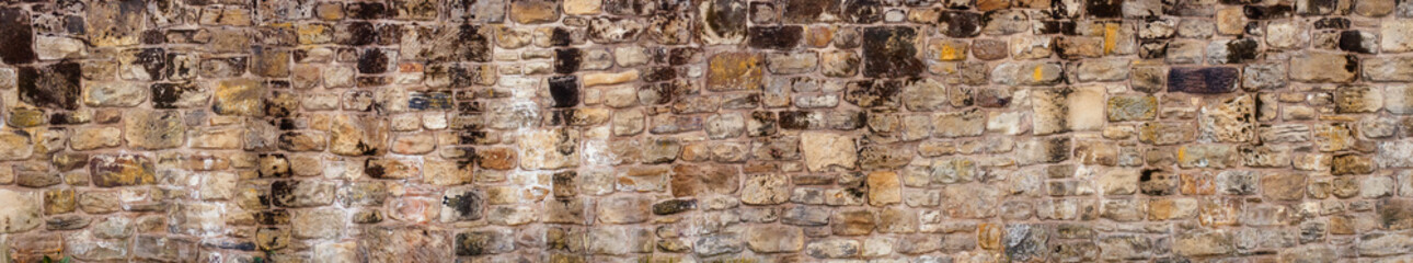 Panoramic of old yellow and brown sandstone wall made of blocks of irregular shape  background