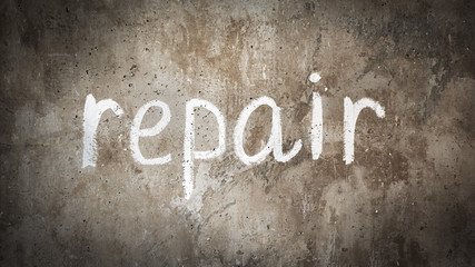 Concrete wall background with text repair. On the wall in white paint is written repair