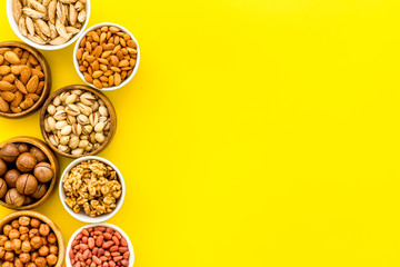 Set of macadamia, hazelnut, walnut, almond, pistachio, pecans nuts on yellow background top-down frame copy space
