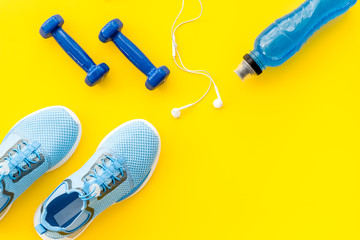 Obraz na płótnie Canvas Sport set with dumbbells and sneakers on yellow background top-down copy space