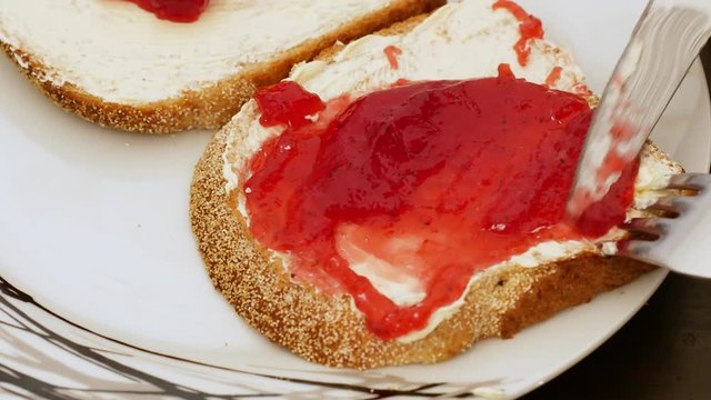 Studio: delicious strawberry jam being spread by silver knife on bread and butter