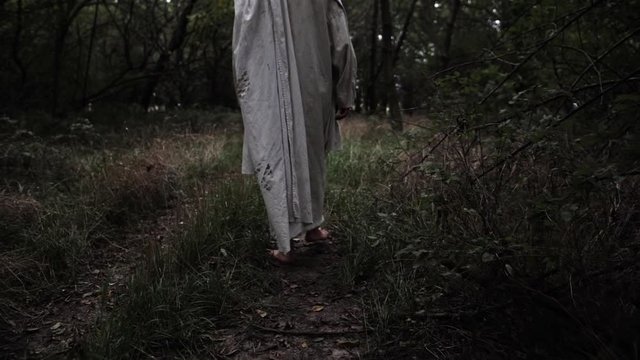 Jesus in white robe walking in slow motion through forest trees.