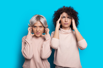 Pensive caucasian women with curly hair touching their head thinking about something and posing on a blue wall