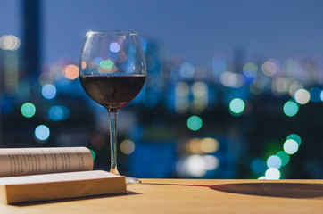 A glass of red wine on wooden table when reading book with colorful bokeh lights. Stay home concept.
