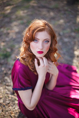 red-haired girl in a burgundy dress walks in the forest