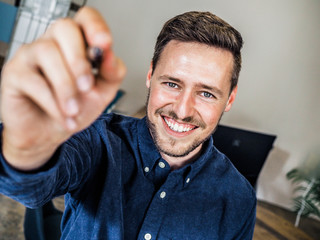 happy smiling man sitting on a chair with a pen in his hand writing  in dark blue shirt